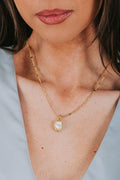 Close-up of a person wearing a gold necklace with a pendant against a light blue background