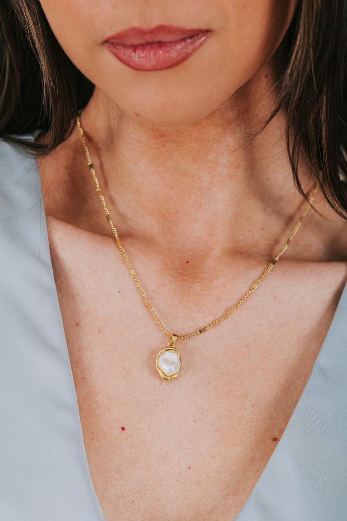 Close-up of a person wearing a gold necklace with a pendant against a light blue background