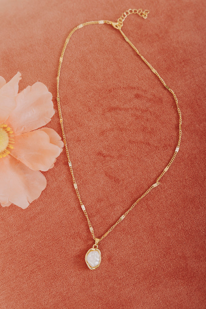 Gold necklace with a pendant on a pink textured background