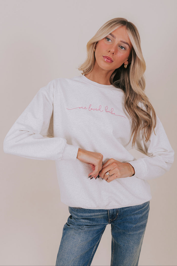 grey sweatshirt with One Loved Babe embroidered in pink on the front/