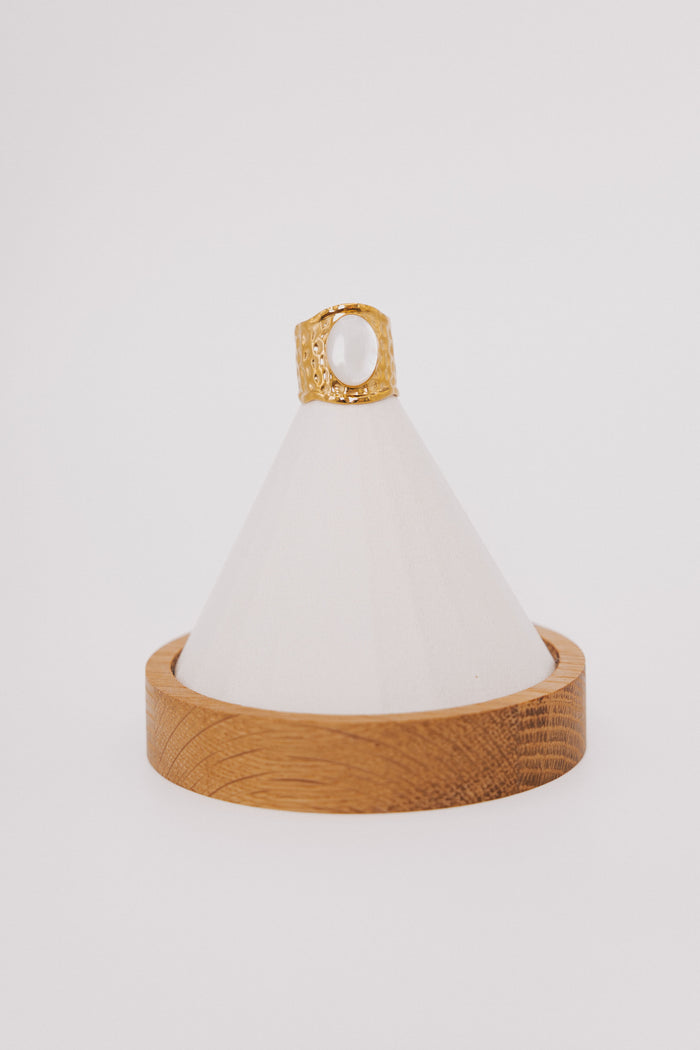 wide gold ring with white stone in center