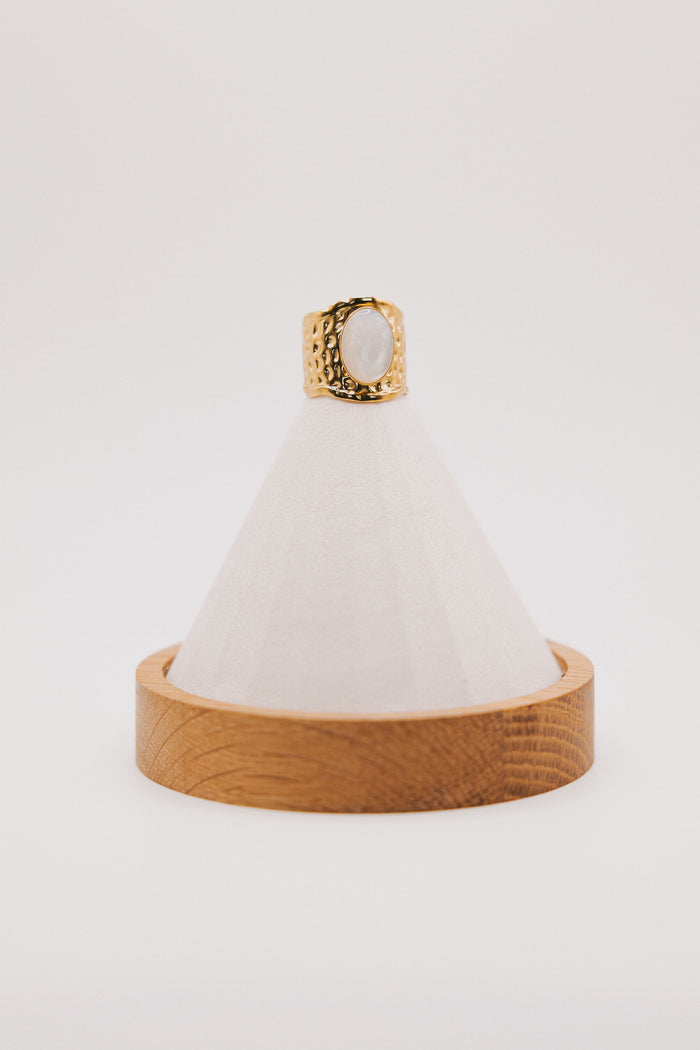 wide gold ring with white stone in center