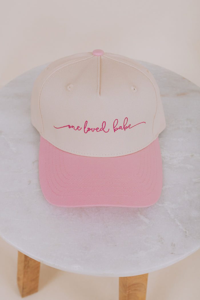 Pink and beige cap with 'one loved babe' text on a marble surface