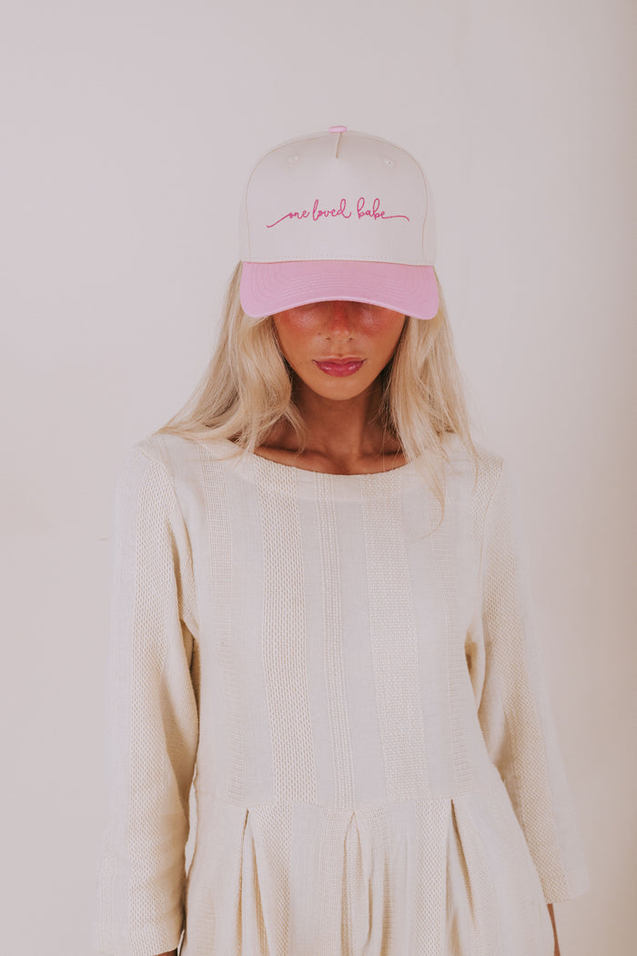 Person wearing a white cap with pink text and a matching pink visor against a plain background