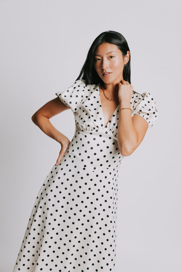 cream and black polka dot dress with v neck and puffed sleeves pose