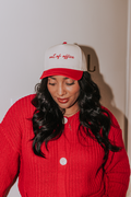 Person wearing a red and white cap with text and a red sweater against a plain background