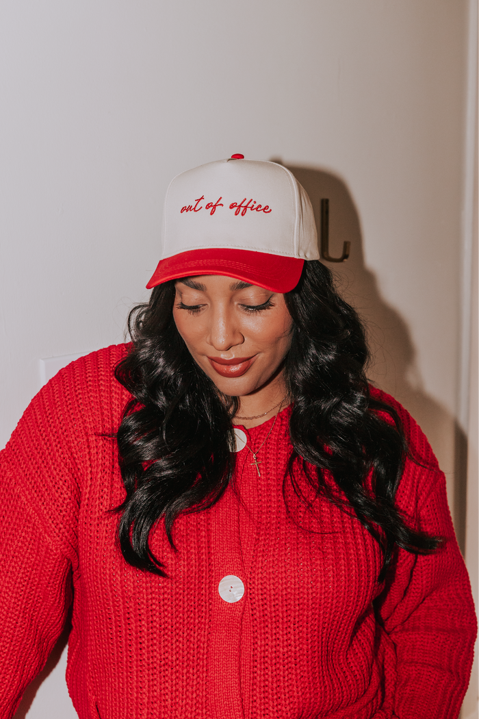Person wearing a red and white cap with text and a red sweater against a plain background