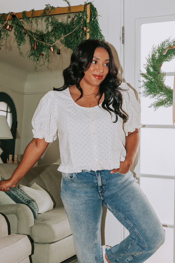 Woman in a white blouse and blue jeans standing in a living room with a wreath on the door.