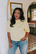 Woman in a yellow top and blue jeans standing in a home interior.