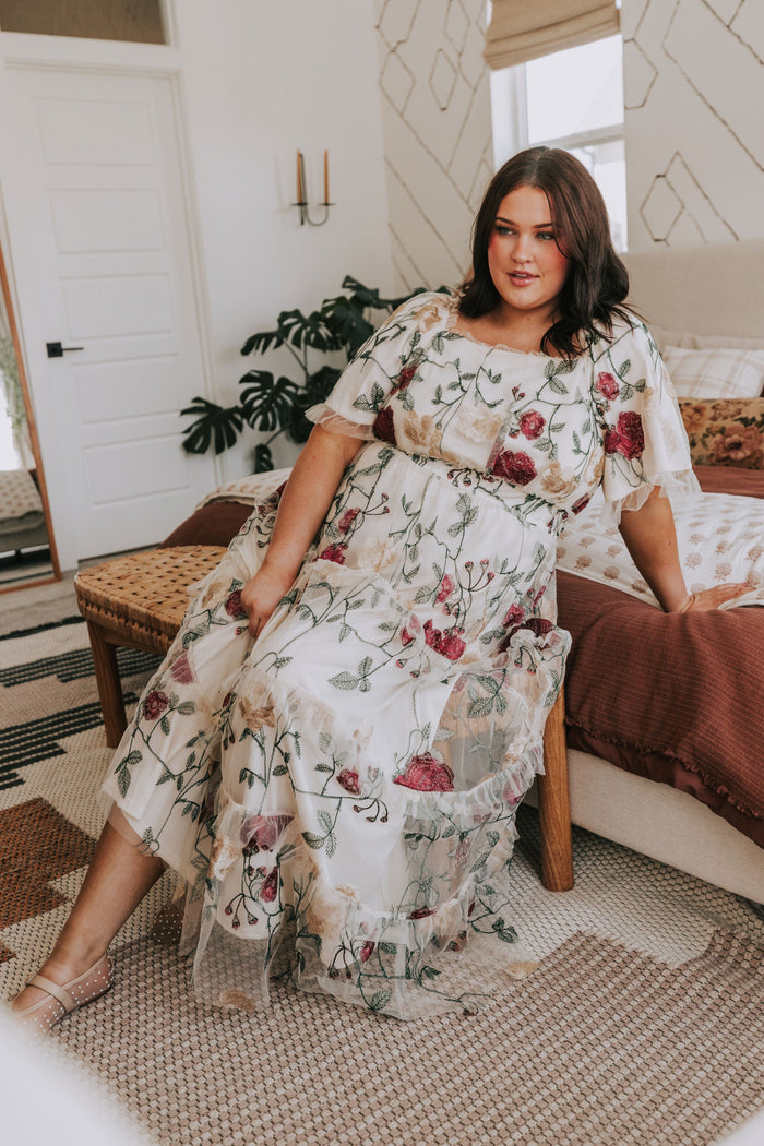 Woman in a floral dress sitting on a bed in a bedroom.