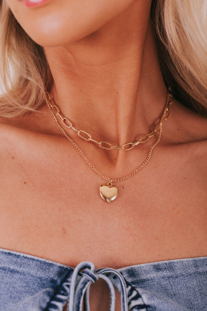 Double layered gold colored necklace with a paper clip chain and a heart pendant.