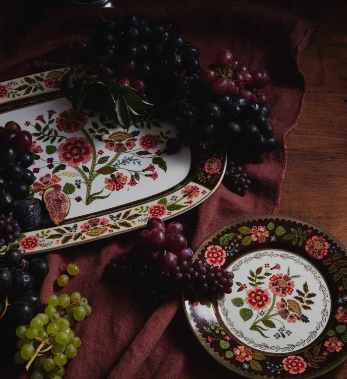Decorative plates with floral designs surrounded by grapes on a wooden surface