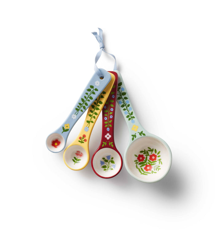 Set of four floral-patterned measuring spoons hanging on a white background