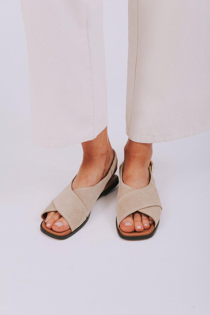 Beige sandals worn with white pants on a light background
