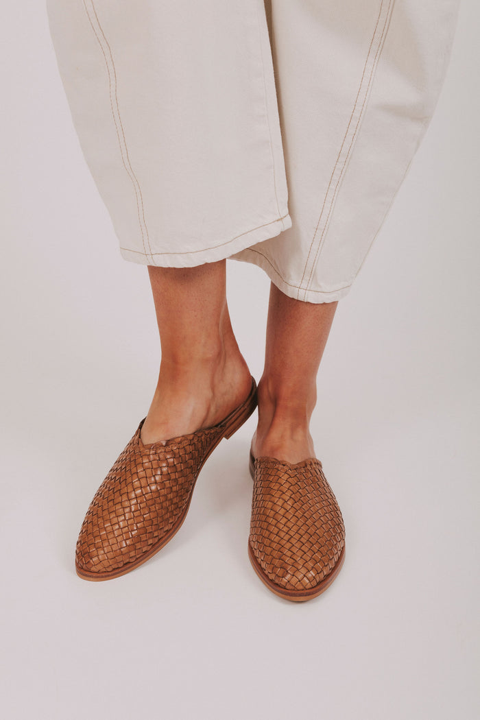 Brown woven shoes worn with light-colored pants on a plain background