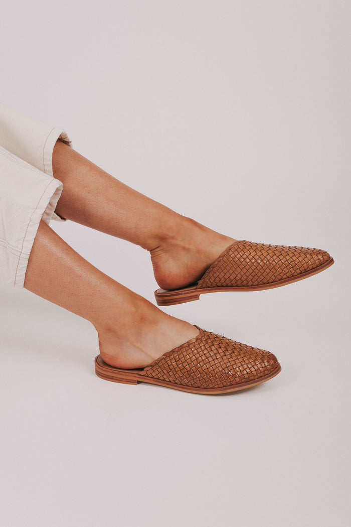 Brown woven flats worn with beige pants on a light background