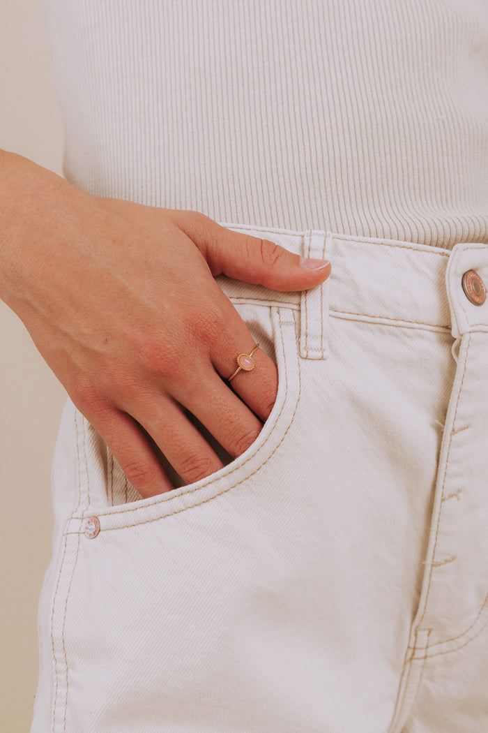 A gold-plated ring with an oval pink stone and textured details, displayed on a model.