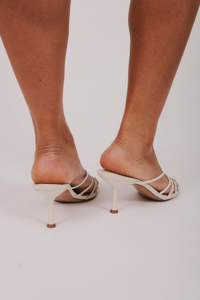White high-heeled shoes worn by a person on a plain background