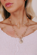 Close-up of a person wearing a gold necklace with a pendant on a light background