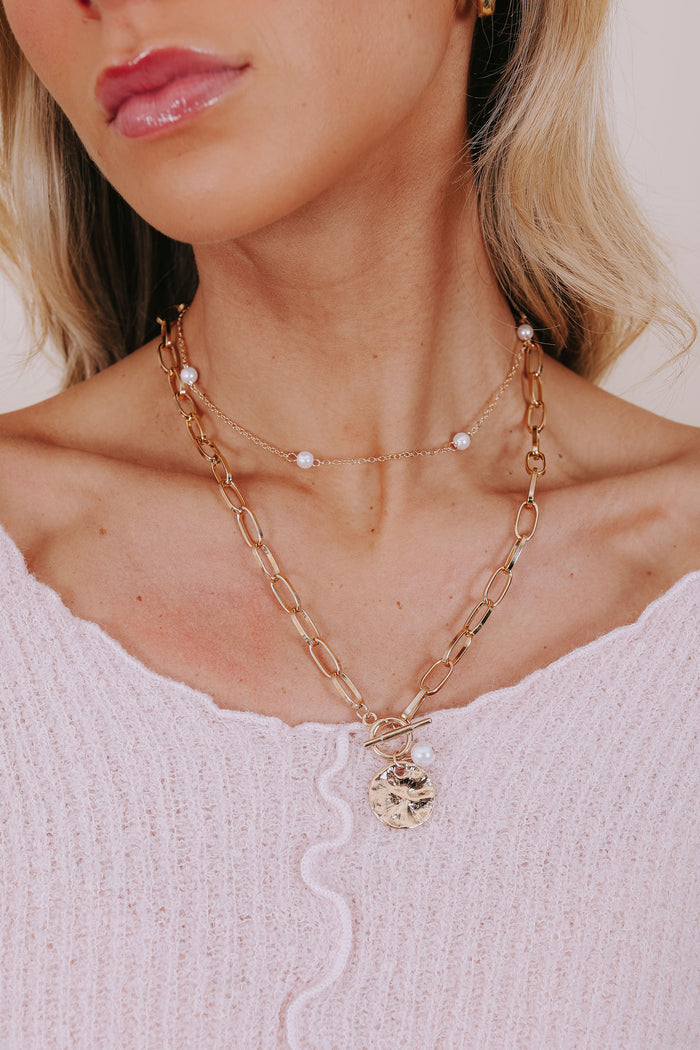 Close-up of a person wearing a gold necklace with a pendant on a light background