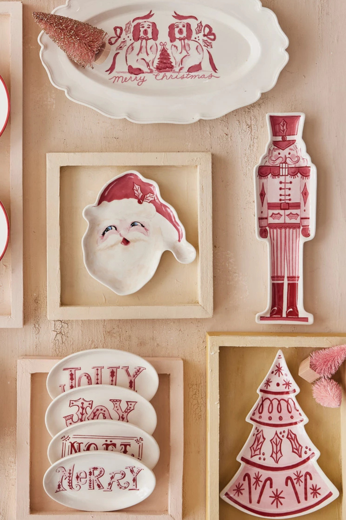 Collection of Christmas-themed ceramic items including a nutcracker, Santa face, and tree on a beige surface.