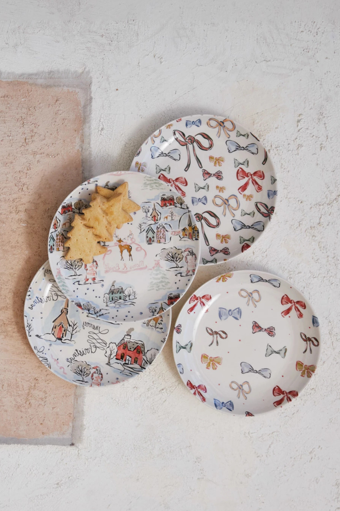 Set of four decorative plates with holiday and bow designs on a light surface.