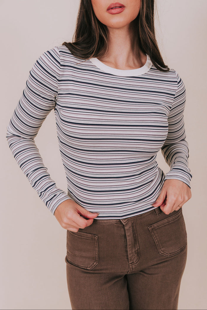 Woman wearing a striped long-sleeve top and brown pants against a plain background