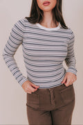 Woman wearing a striped long-sleeve top and brown pants against a plain background