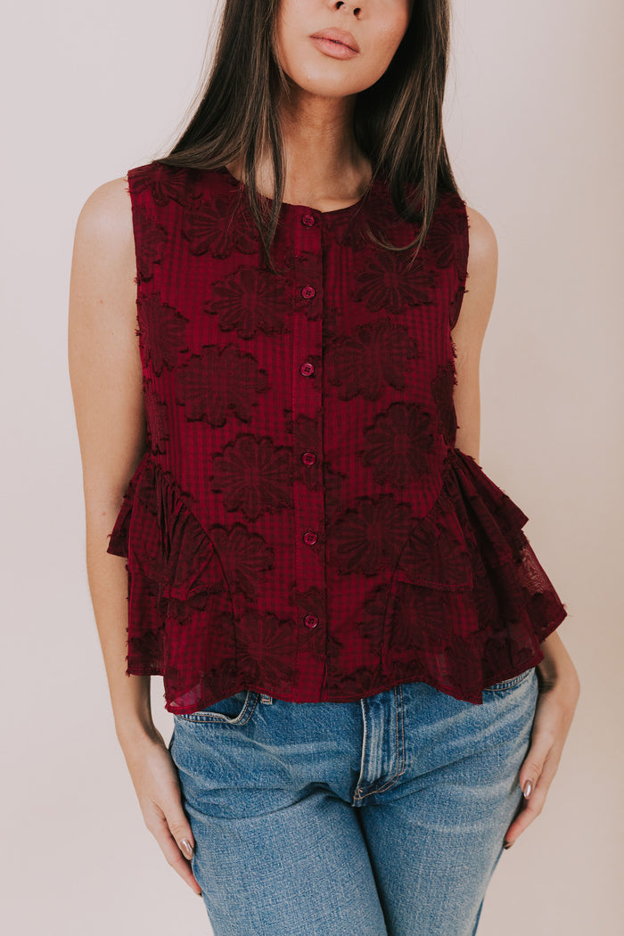 Woman wearing a red lace peplum top and blue jeans against a plain background