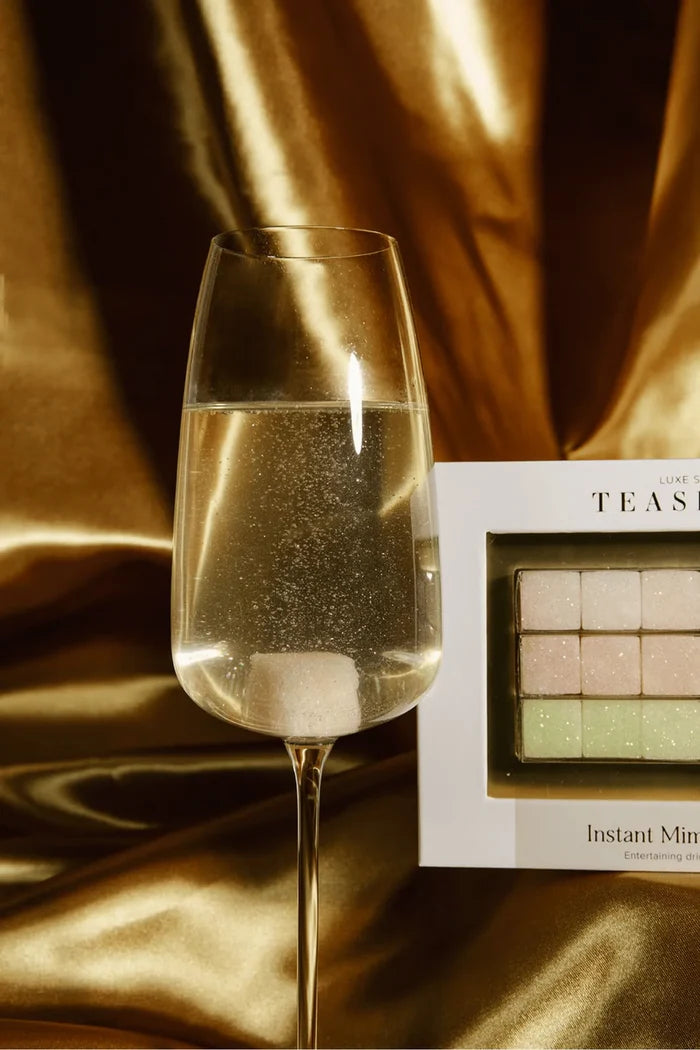 A closeup of a luxe sugar cube dissolving in a glass of champagne where you can also see the sparkles.