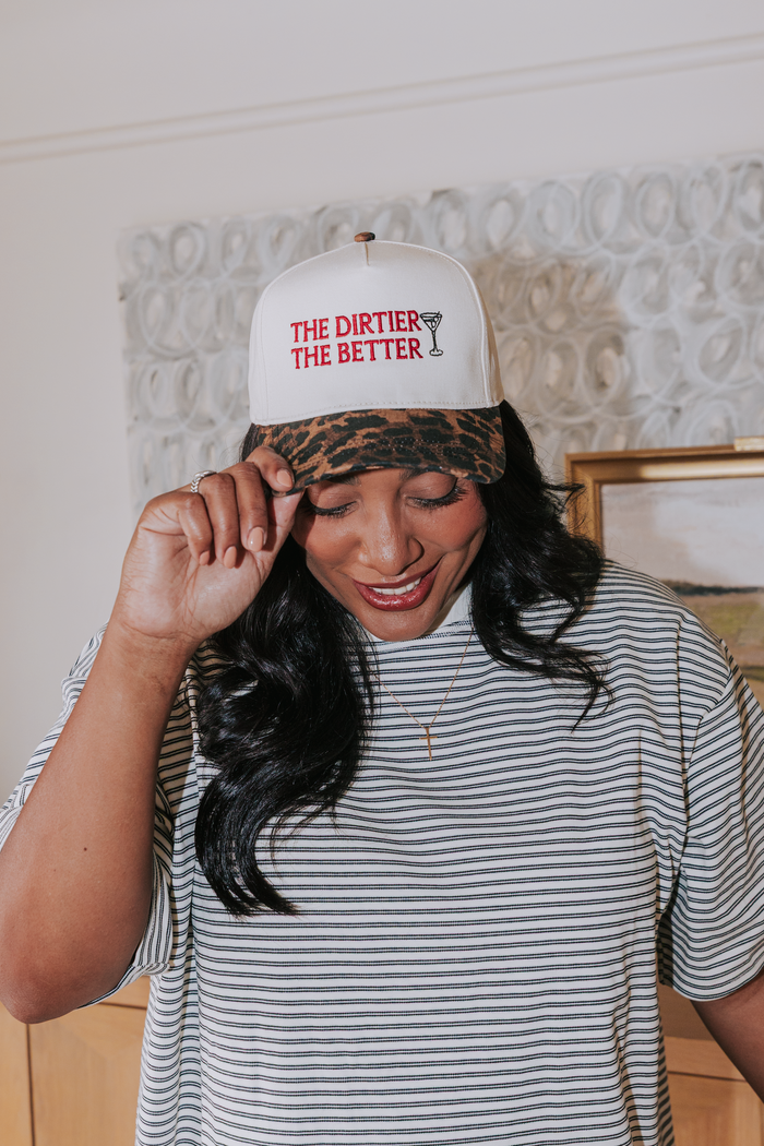 Woman wearing a striped shirt and a cap with text, standing indoors.