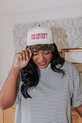 Woman wearing a striped shirt and a cap with text, standing indoors.