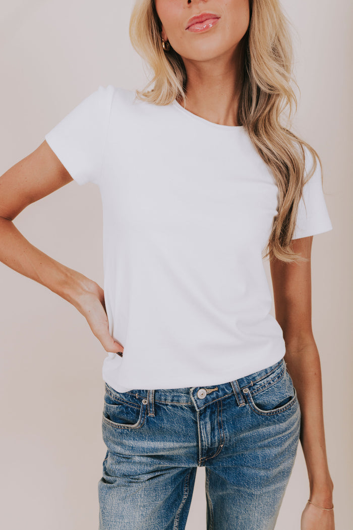 Woman wearing a plain white t-shirt and blue jeans against a neutral background